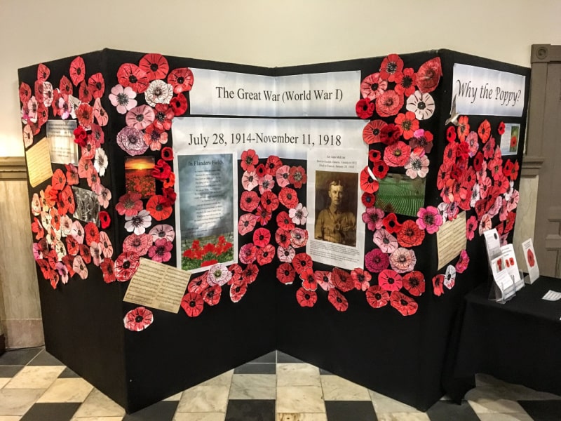 Photograph of a black display board covered with red poppies made from paper and crocheted yarn.